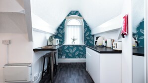 Une cuisine étroite avec une fenêtre, des murs blancs et un pare-feu décoré de motifs de feuilles.