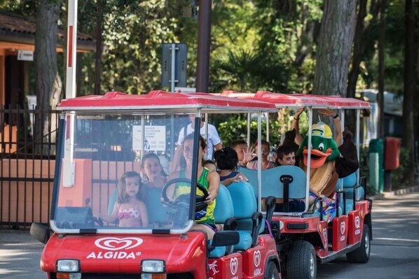 A red tour vehicle with a mascot character, passengers, and a visible logo.