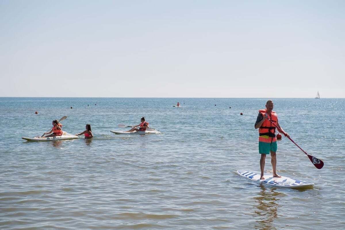 A person standing on a paddleboard in the water, with others paddling nearby.