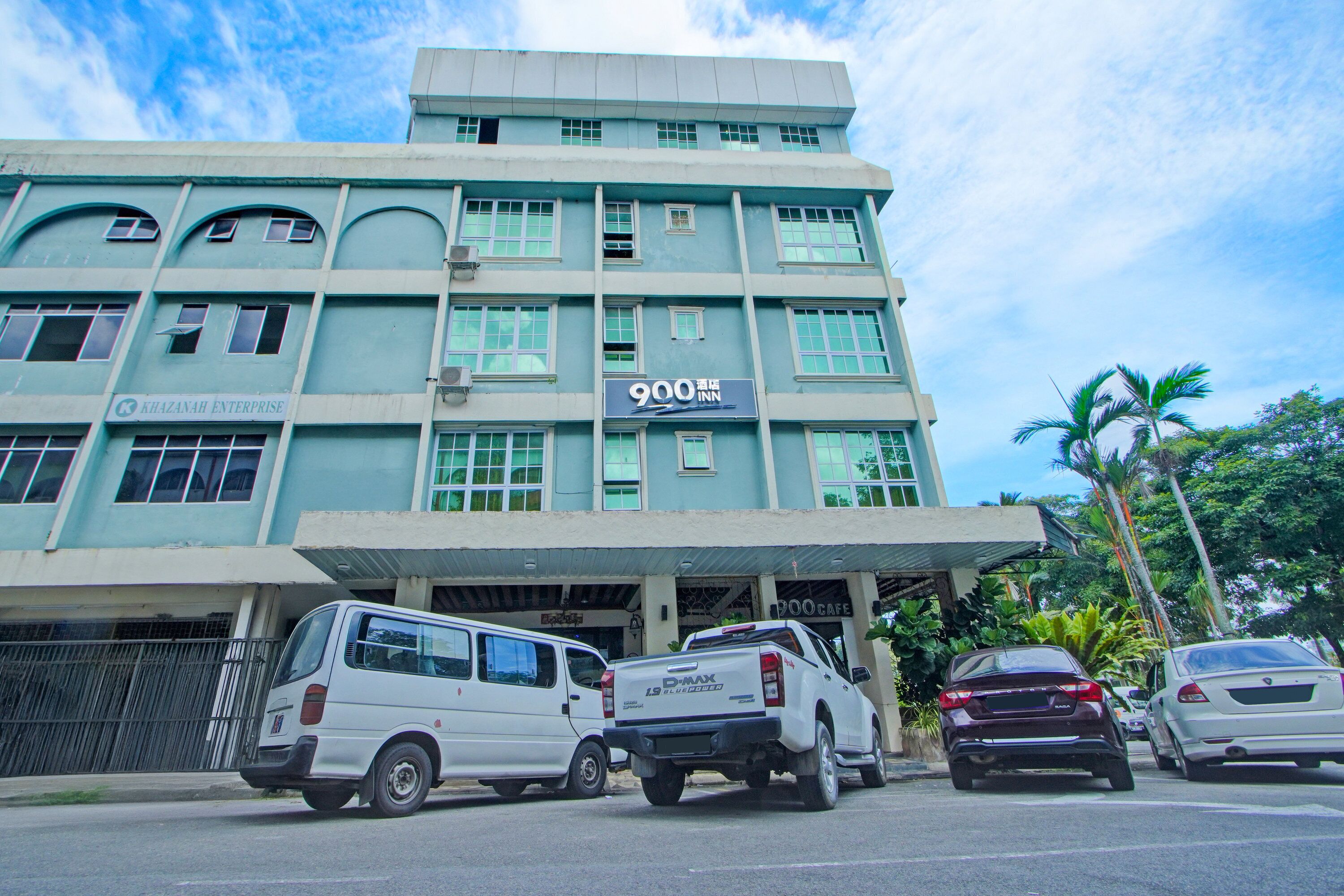 A multi-story building with a sign for '900 Inn' and 'Khazanah Enterprise' on the facade. There are parked vehicles in front.