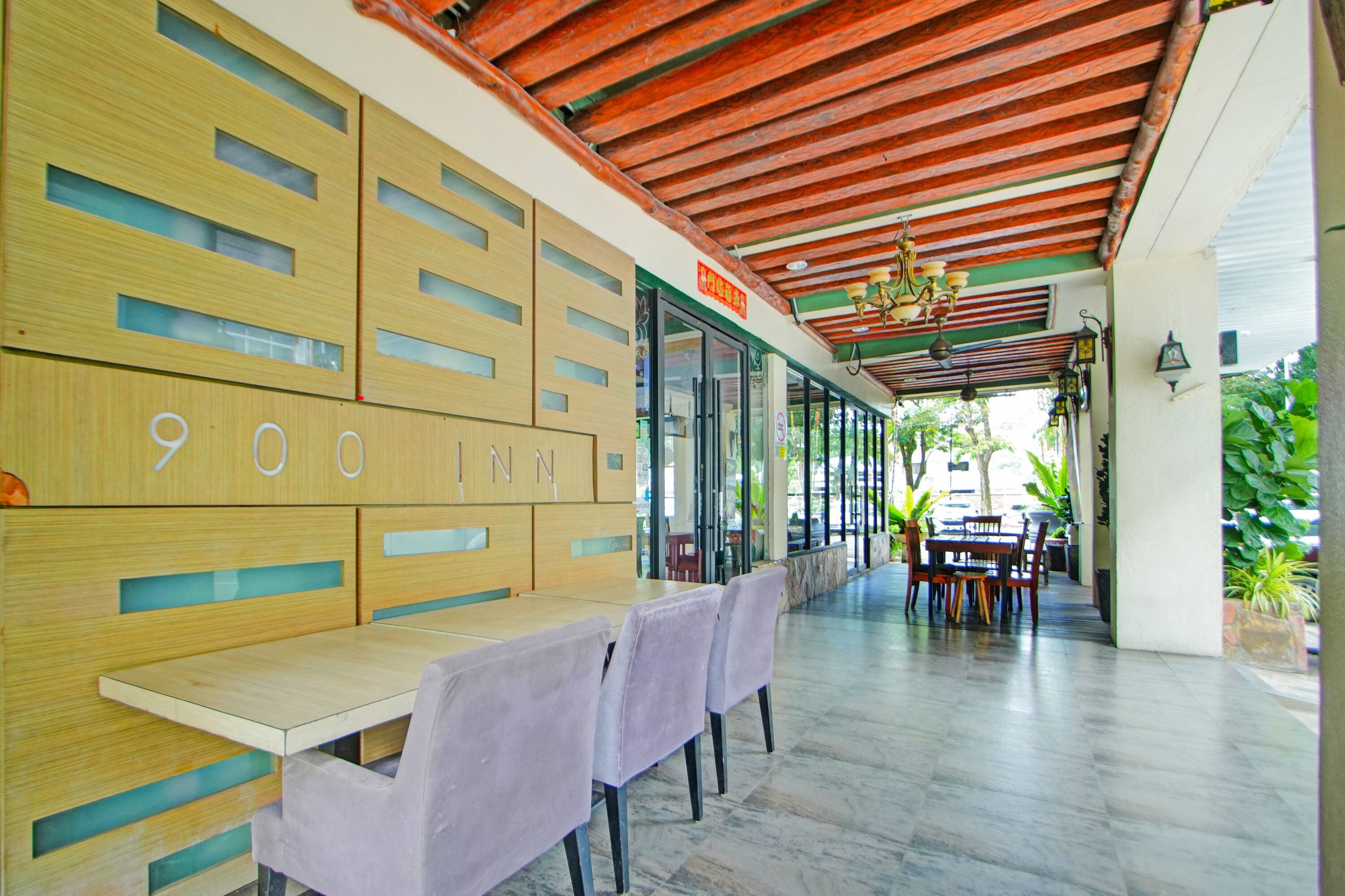 A hotel lobby with a wooden reception desk, a seating area with tables and chairs, and a view of the outdoors.