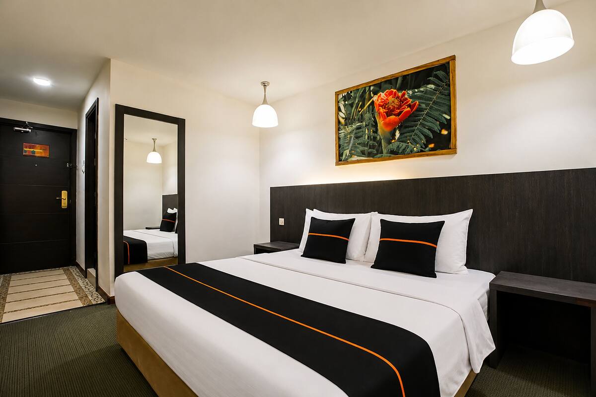 Una habitación de hotel con una cama grande, una mesita de noche, un espejo y un cuadro en la pared.