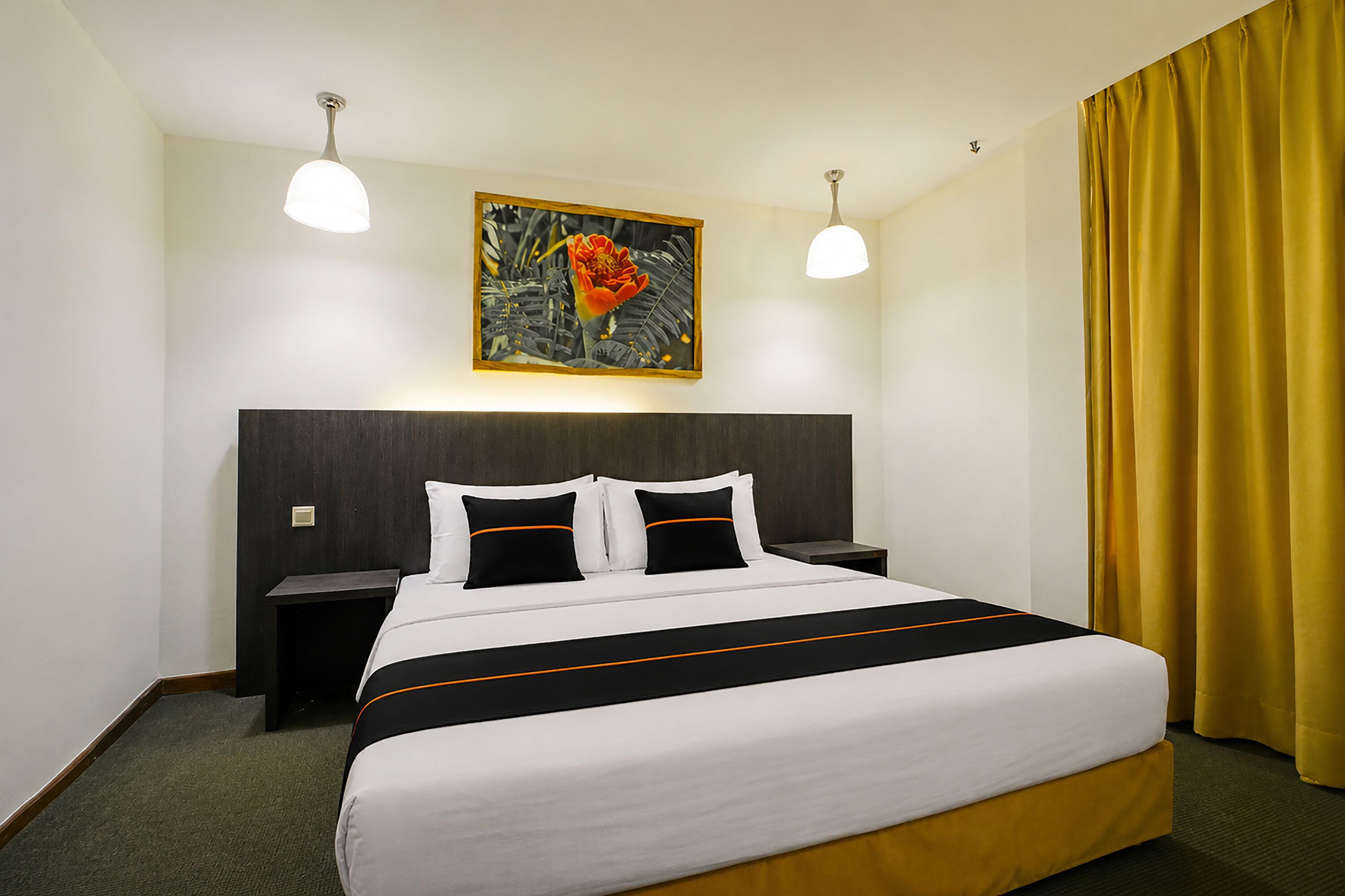 Een hotelkamer met een groot bed, twee nachtkastjes, een schilderij aan de muur en een geel gordijn.