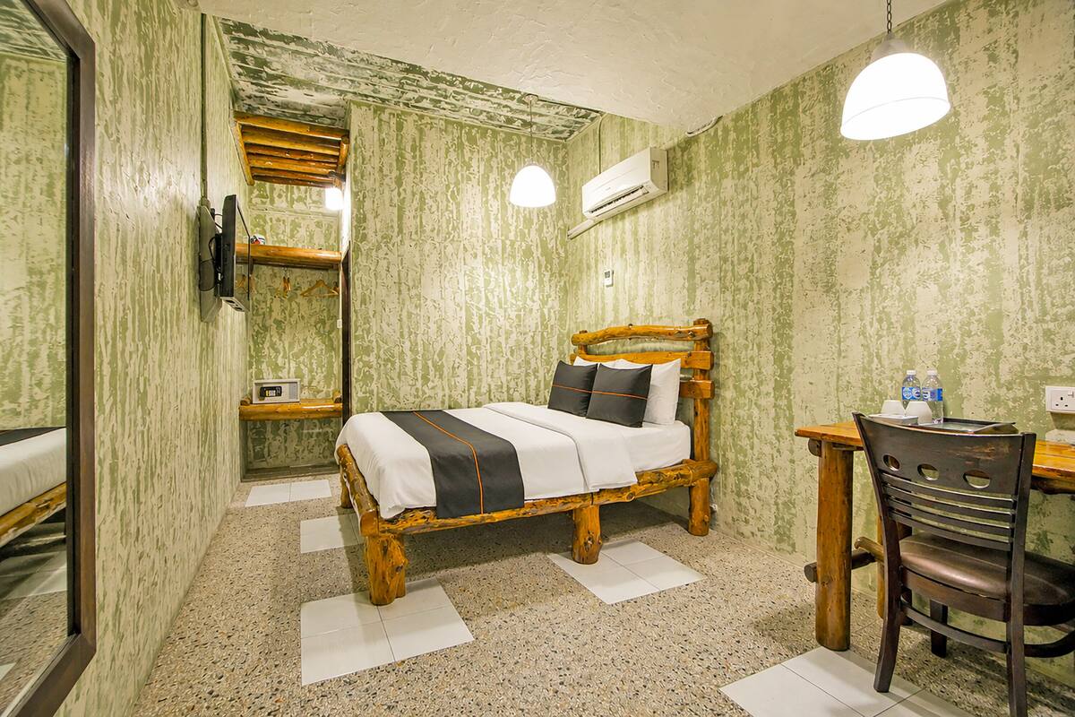 Una habitación con cama, escritorio, silla, espejo y aire acondicionado.