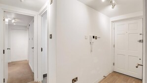 Een gang met witte wanden, een houten vloer, een deur met een greep en een lichtschakelaar op de muur.