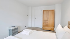 Een slaapkamer met een bed, een houten kledingkast, een wasmand en een deur.