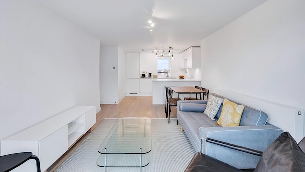 Een moderne woonkamer met een bank, een glazen salontafel en een eethoek met stoelen.