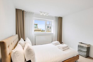 Ein Hotelzimmer mit Bett, Vorhängen, einem Fenster mit Blick auf Gebäude und einem Heizkörper.