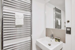 Ein Badezimmer mit chromfarbenem Handtuchhalter, einem Spiegel, einem Waschbecken und Pflegeprodukten.