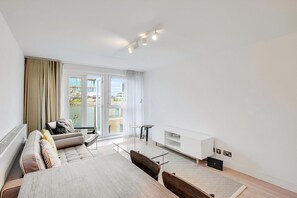 Ein modernes Hotelzimmer mit einer Couch, einem Glastisch, einem kleinen Fernseher und einer Schiebetür zum Außenbereich.