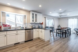 A modern kitchen with white cabinets, a stainless steel dishwasher, and a dining area with a table and chairs. - Lakeview Cabin w/Walk to Lake + Slopes + Dog (Big Bear Lake)