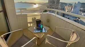 En balkon med et bord, to stole og udsigt til både strand og bybillede.