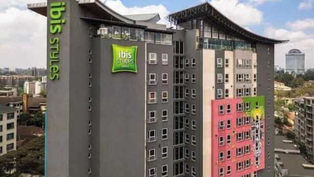Ein Hochhaus mit mehreren Balkonen, einem gut sichtbaren, grünen 'ibis Styles'-Schild und Blick auf die Stadtlandschaft.