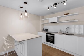 Eine moderne Küche mit weißen Schränken, einem Backofen, einer Spüle und Pendelleuchten.