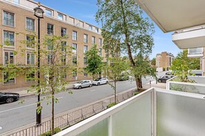 A residential building with multiple windows, a street with parked cars, and a tree in the foreground. - Belgravia Living First Floor 2-bed With Balcony (London)