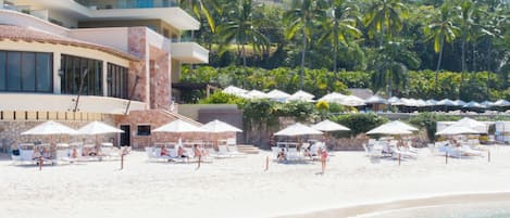 Een strandhotel met meerdere balkons, een zandstrand en palmbomen.