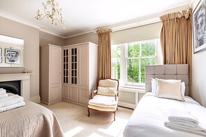 Um quarto com cama, uma cadeira, guarda-roupa, lareira e janela com cortinas.