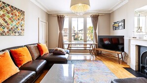 A living room with a sofa, TV, fireplace, and large windows. - Super Chic 1-bedroom Urban Hideaway (Twickenham)