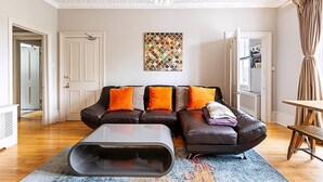 A living room with a sectional sofa, a coffee table, a chandelier, and a colorful rug. - Super Chic 1-bedroom Urban Hideaway (Twickenham)