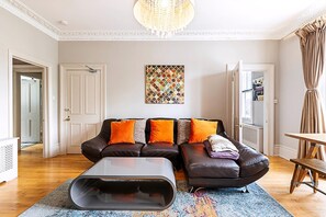 Ein Wohnzimmer mit einem Ecksofa, einem Couchtisch, einer Kristallleuchtre und einem farbenfrohen Teppich.