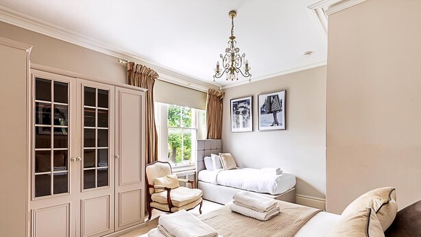 A bedroom with a bed, a chair, a wardrobe, and a chandelier. - Super Chic 1-bedroom Urban Hideaway (Twickenham)