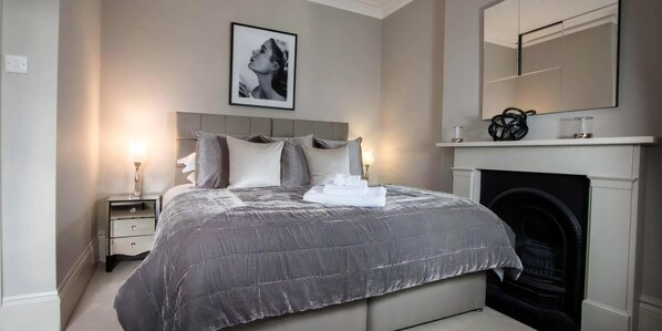 A bedroom with a bed, bedside tables, a fireplace, and a framed picture on the wall. - Super Chic 1-bedroom Urban Hideaway (Twickenham)