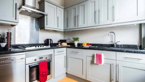 A modern kitchen with stainless steel appliances, grey cabinetry, and a black countertop. - Super Chic 1-bedroom Urban Hideaway (Twickenham)