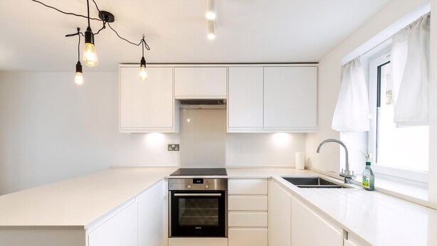 A compact kitchen with white cabinetry, a built-in oven, a sink, and pendant lighting. - Belgravia Living 2-bed, 2-bath Home With Balcony (London)