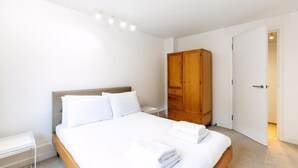 A neatly made bed with white linens, a wooden wardrobe, and a bedside table with a lamp. - Belgravia Living 2-bed, 2-bath Home With Balcony (London)