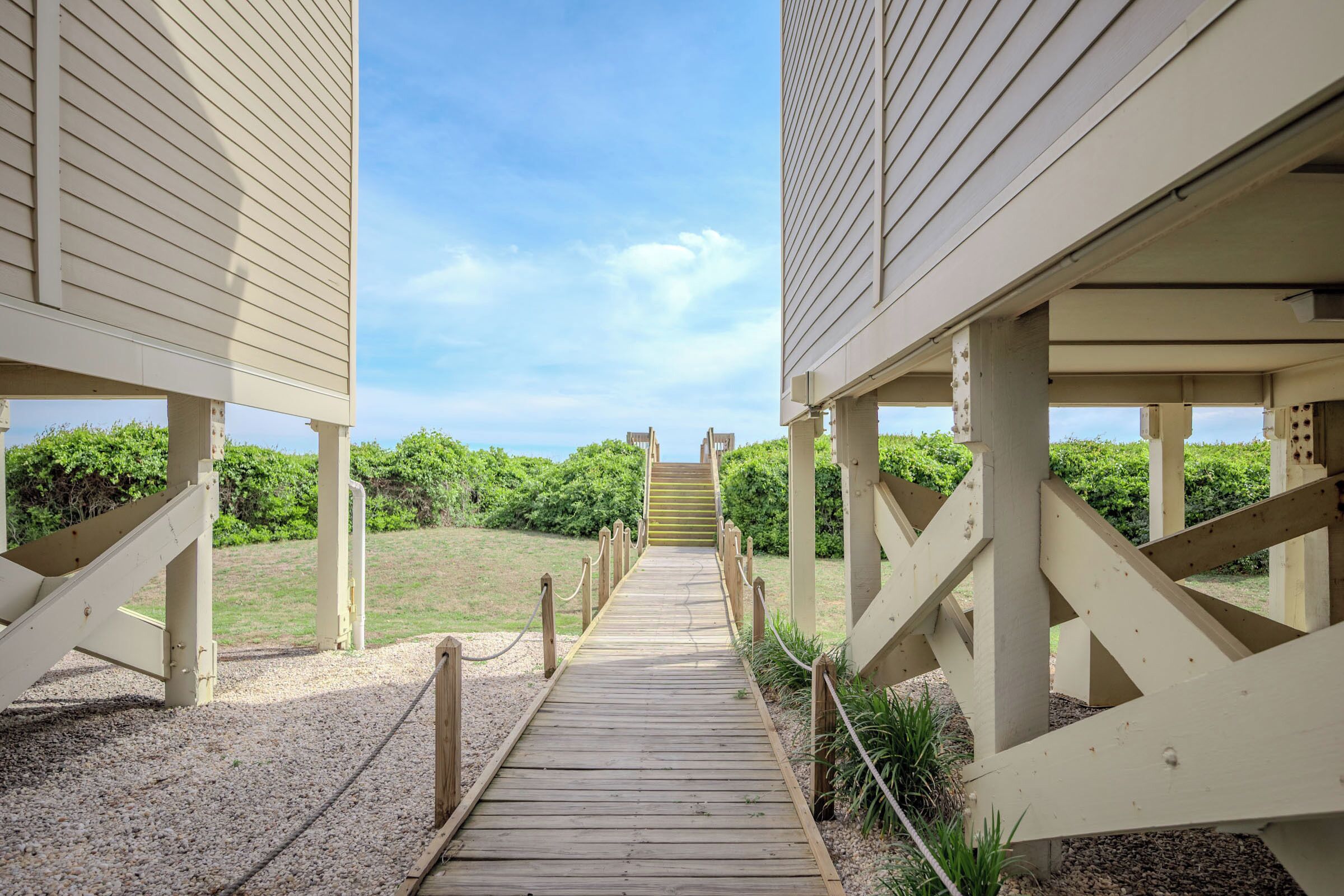 A wooden pathway leading to a building with a clear view of the sky and greenery.