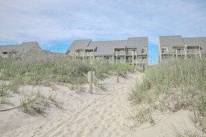 Ein Strandhotel mit mehrstöckigen Gebäuden, einem sandigen Weg zum Eingang und üppiger Vegetation.
