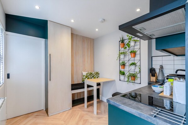 A modern kitchen with a built-in stove, a dining area with a bench, and a wall-mounted plant shelf. - The Balham Hideaway (London)
