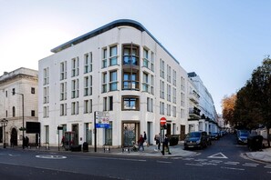 Ein modernes Gebäude mit einer gewölbten Fassade, zahlreichen Fenstern und einem Schild, das auf eine nahegelegene Sehenswürdigkeit hinweist.
