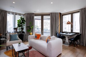 Ein modernes Wohnzimmer mit Sofa, Sessel, Esstisch und Topfpflanzen.
