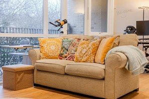 Ein gemütliches Wohnzimmer mit einer Couch, einem Hocker und einem Teleskop auf einem Tisch.
