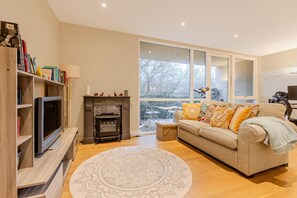 Ein Wohnzimmer mit Fernseher, Bücherregalen, einer Couch und Blick ins Freie.