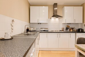 Eine moderne Küche mit weißen Schränken, einer Edelstahl-Dunstabzugshaube, einem Spülbecken, einem Toaster und einer Kaffeemaschine.