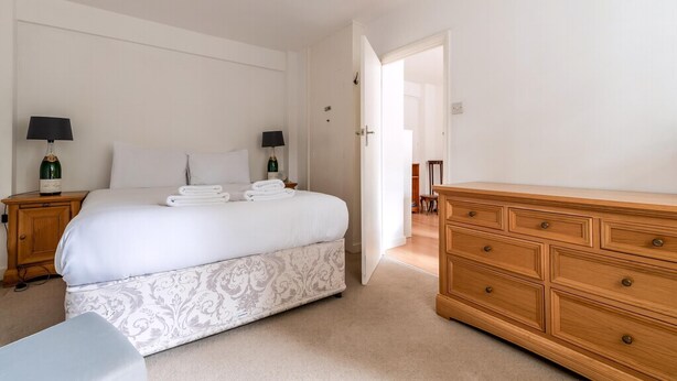 Quarto com uma cama, duas mesas de cabeceira com luminárias, um aparador de madeira e uma porta que dá para outro cômodo.