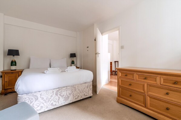 A bedroom with a bed, two bedside tables with lamps, a wooden dresser, and a door leading to another room. - Gorgeous Putney Flat (London)