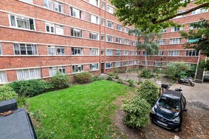 A multi-story brick building with a courtyard, a car, and a scooter parked outside. - Gorgeous Putney Flat (London)