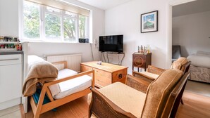 Quarto com cama, mesa de madeira, televisão, sofá e janela com persianas.