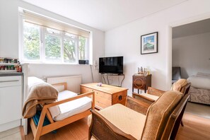 A room with a bed, a wooden table, a TV, a sofa, and a window with blinds. - Gorgeous Putney Flat (London)
