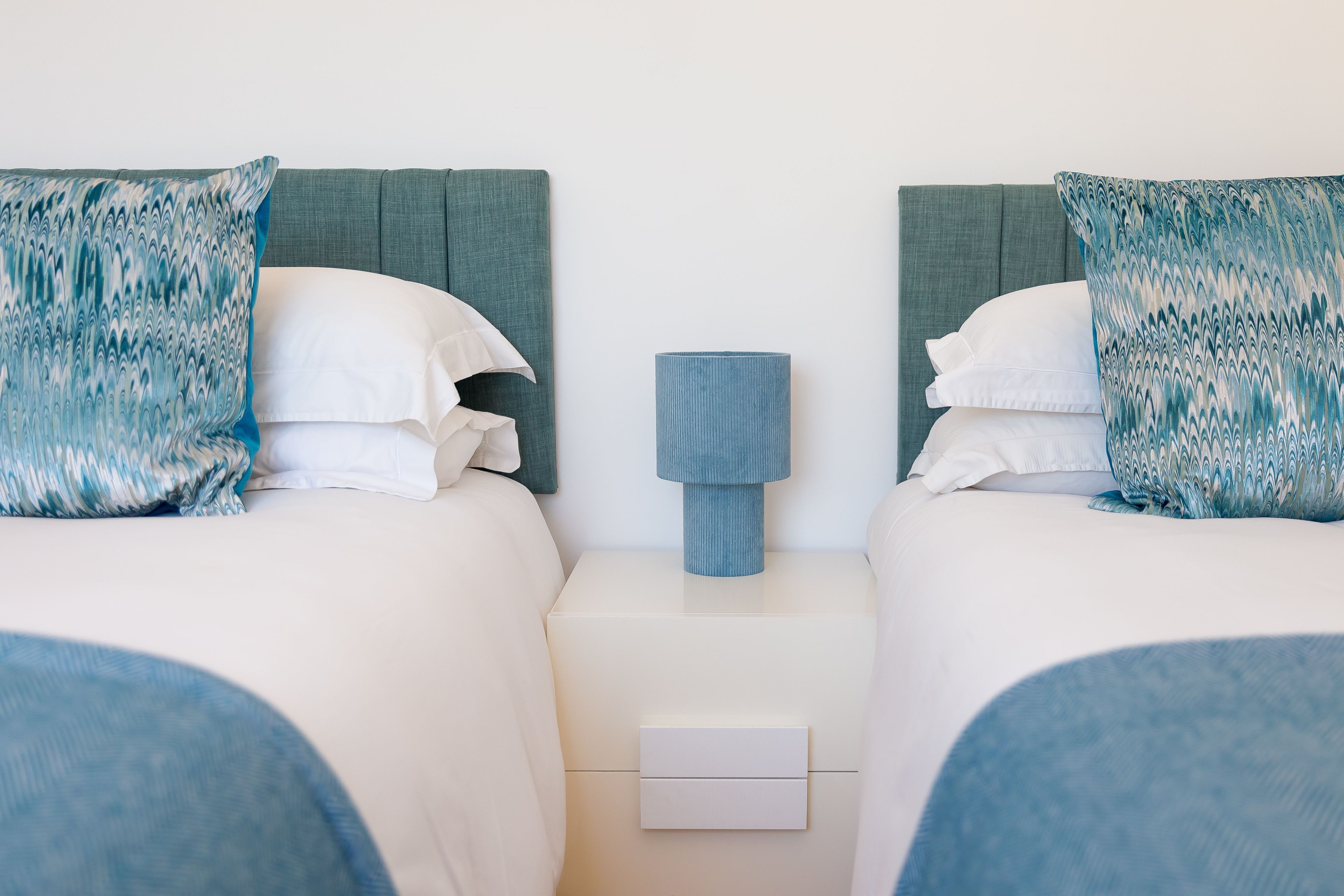 A twin room with two beds, a nightstand with a lamp, and a drawer.
