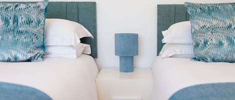 Habitación doble con dos camas, una mesita de noche con lámpara y un cajón.