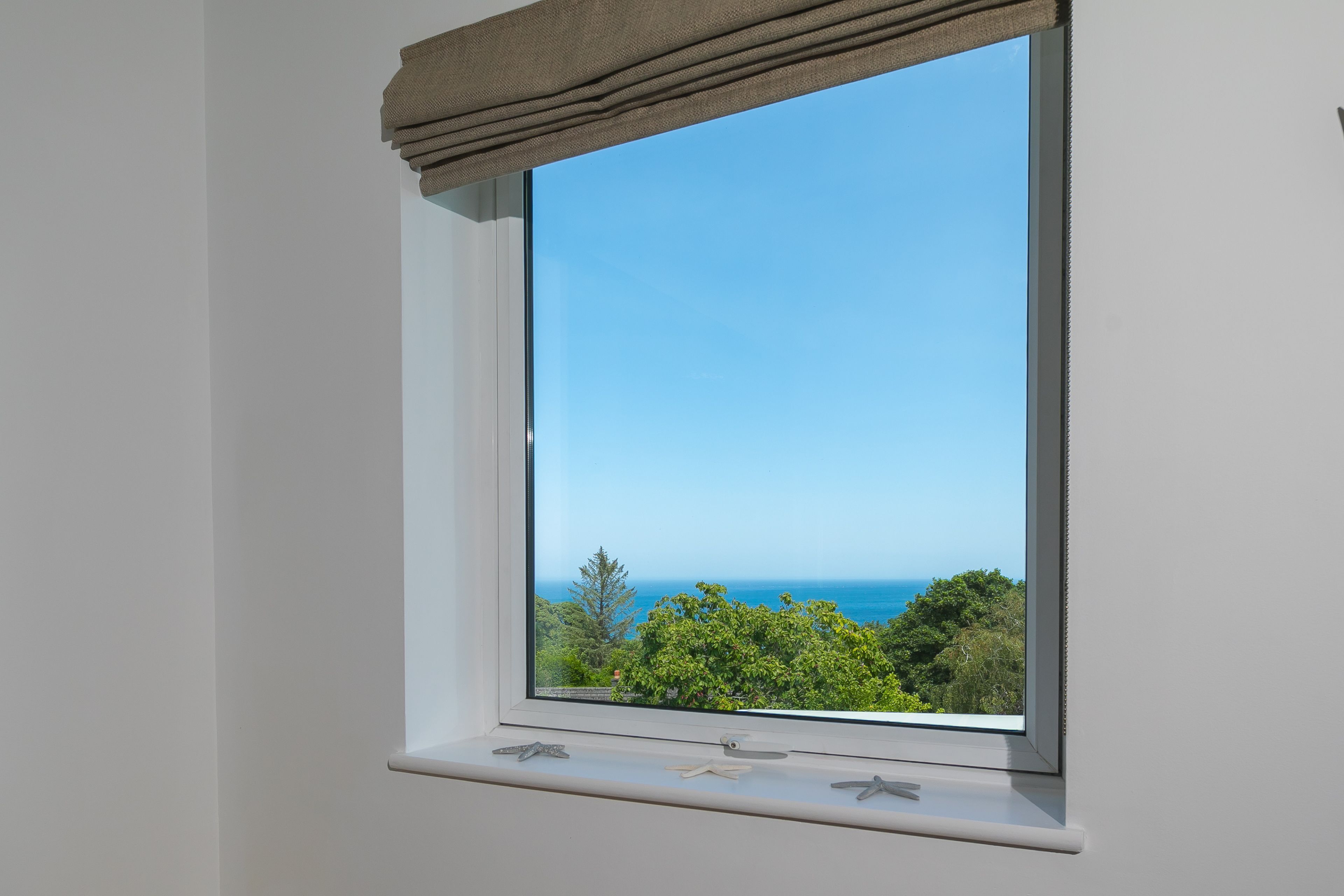 Ein Fenster mit Blick auf das Meer und Bäume.