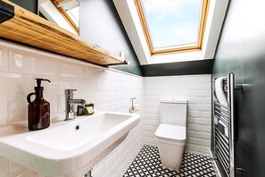 A modern bathroom with a skylight, a large sink, a toilet, and a black and white patterned floor. - Stylish Family Home With Garden in Peckham Rye (London)