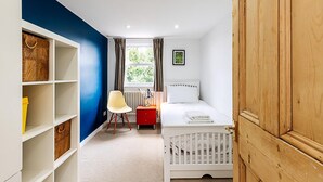 A bedroom with a white crib, a red nightstand, a white chair, a window with curtains, and a blue wall. - Stylish Family Home With Garden in Peckham Rye (London)