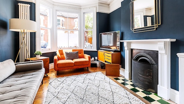 A living room with a sofa, armchair, fireplace, television, and a large window. - Stylish Family Home With Garden in Peckham Rye (London)
