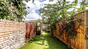 A narrow backyard with a brick wall, a wooden fence, and a small shed. - Stylish Family Home With Garden in Peckham Rye (London)