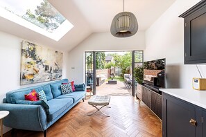 A modern living space with a sofa, ottoman, artwork, and a TV. - Stylish Family Home With Garden in Peckham Rye (London)